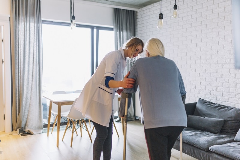 Verpleegkundige helpt een oudere vrouw met krukken.